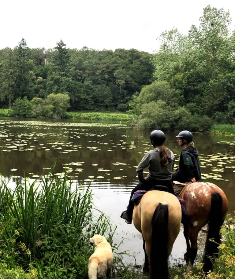 Deux jeunes filles à cheval lors d'une randonnée équestre, faisant face à une rivière